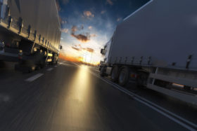 Two HGV trucks driving side by side into the sunset